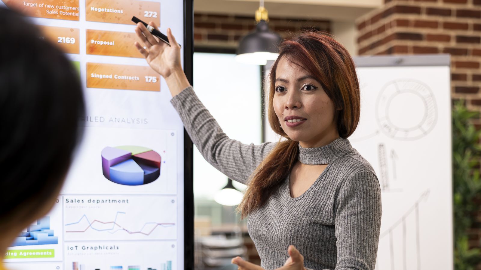 A consultant presenting a sales and analytics dashboard on a screen to a colleague